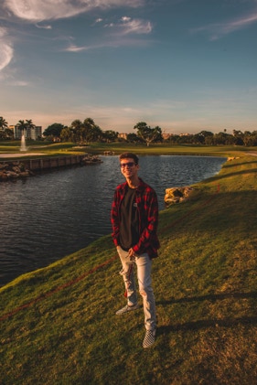 Young man standing on green grass standing in front a bay under a clear, beautiful Florida sky. Photographed by Tiago with the Shots.